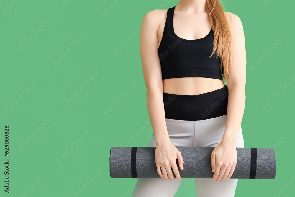 Young woman in sportswear and with yoga mat on green background