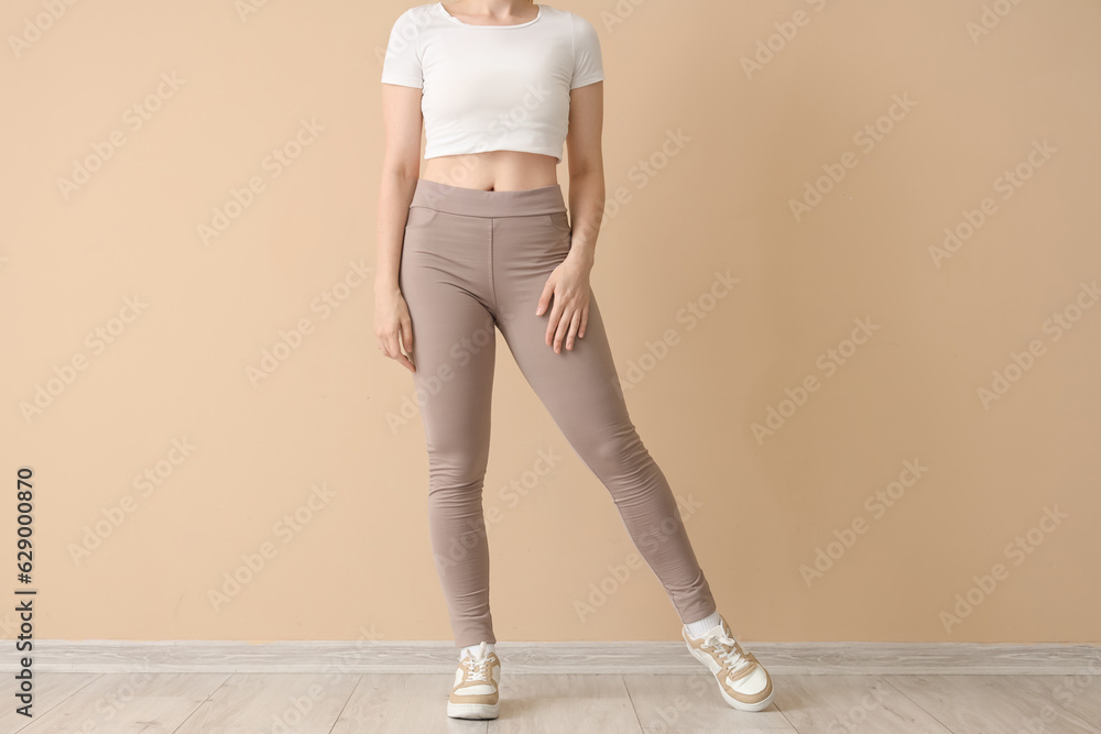 Young woman in sportswear near beige wall