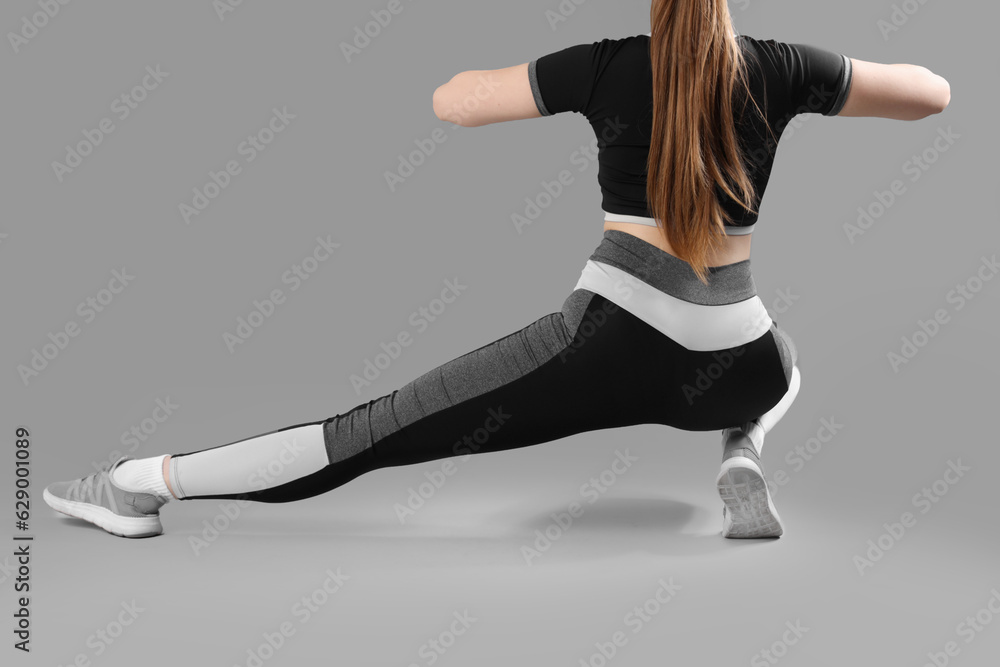 Young woman in sportswear on grey background, back view