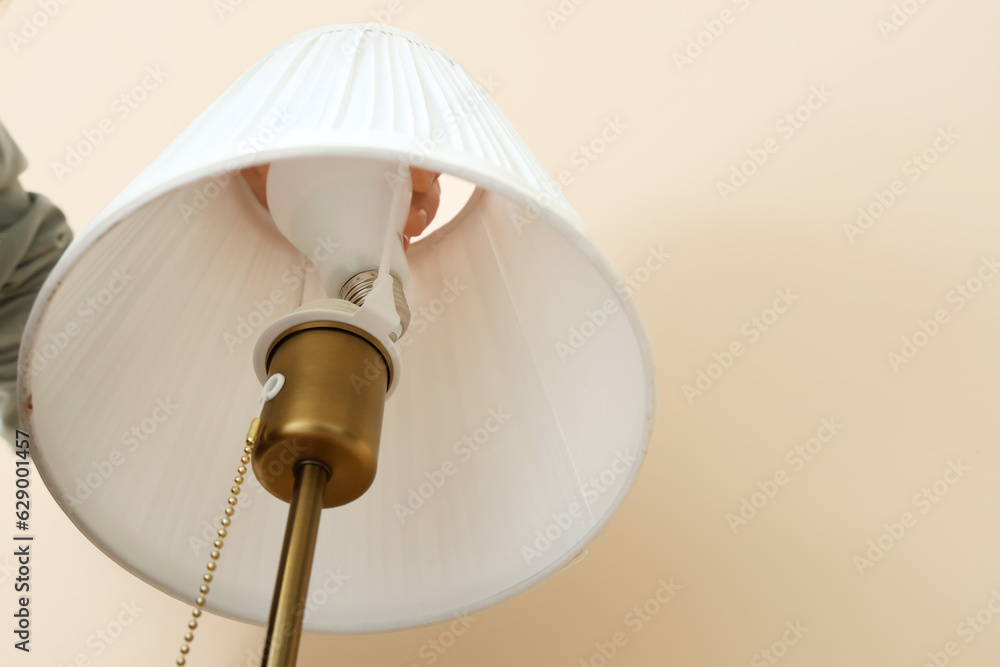 Woman changing light bulb in lamp on beige background, closeup