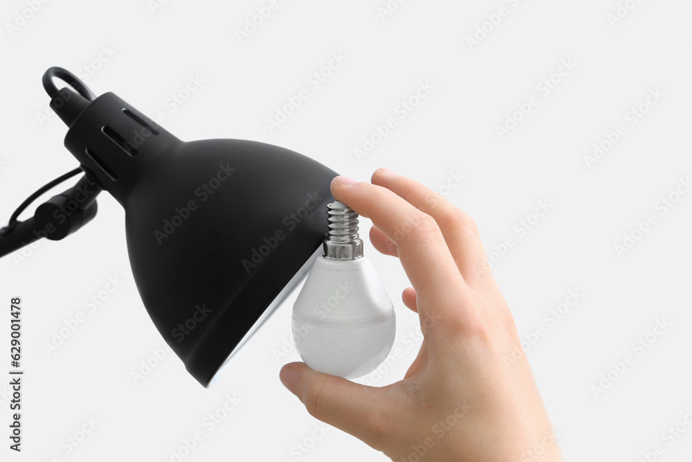 Woman changing light bulb in lamp on light background, closeup