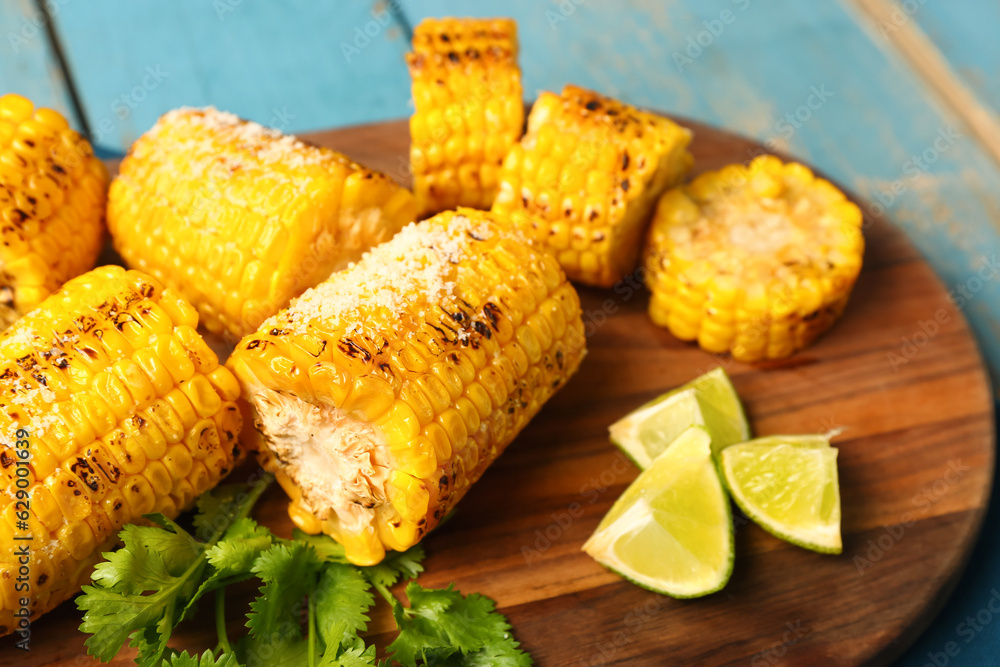 Board with cut tasty grilled corn cobs and parsley on blue wooden background, closeup