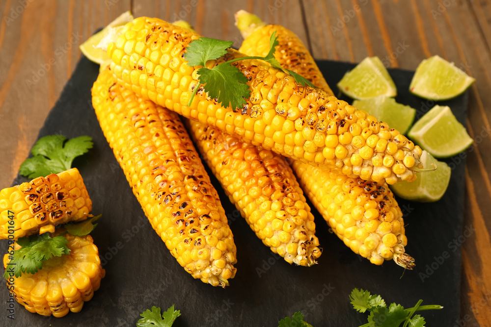 Board with tasty grilled corn cobs and lime on wooden background