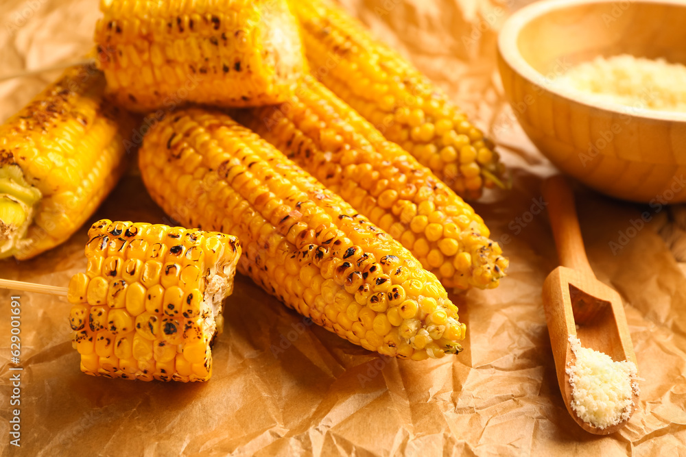 Baking paper with tasty grilled corn cobs and bowl of cheese, closeup