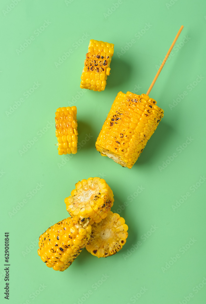 Cut tasty grilled corn cobs on green background