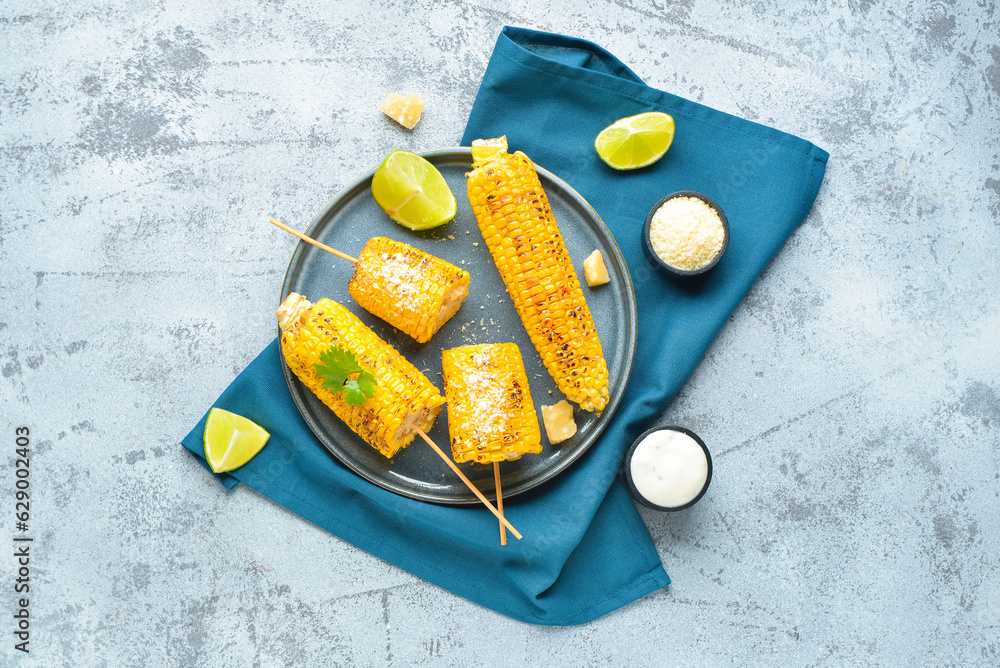 Plate with tasty grilled corn cob skewers and cheese on blue background