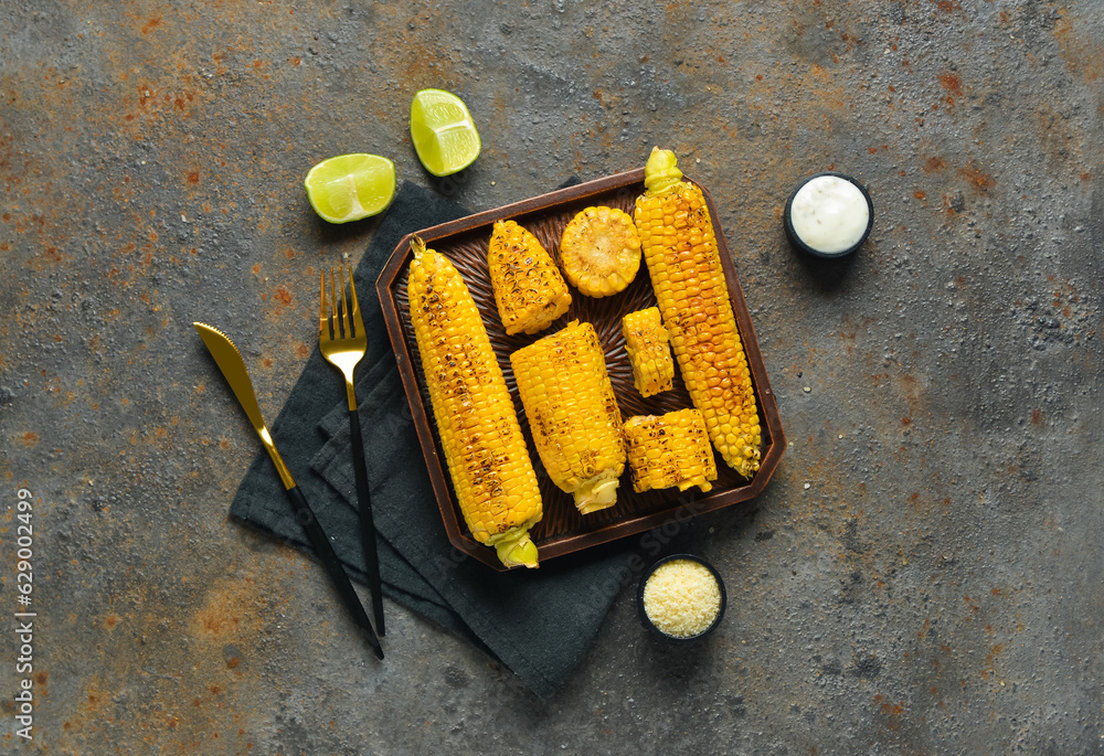 Tray with tasty grilled corn cobs and lime on dark background