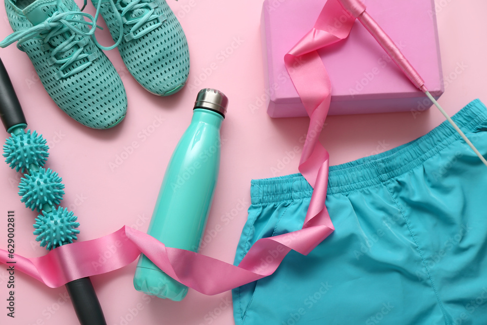 Composition with sports equipment, bottle of water and clothes on pink background