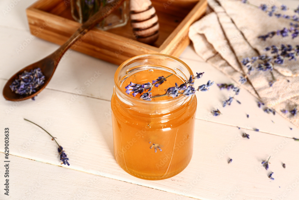 Jar of sweet lavender honey and flowers on white wooden table