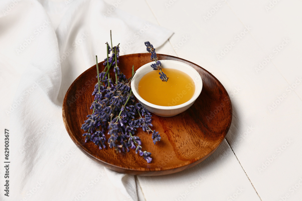 Plate with bowl of sweet lavender honey and flowers on white wooden background