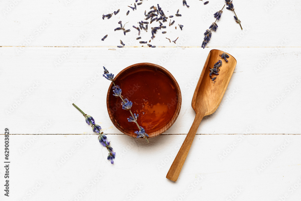 Bowl of sweet lavender honey and flowers on white wooden background