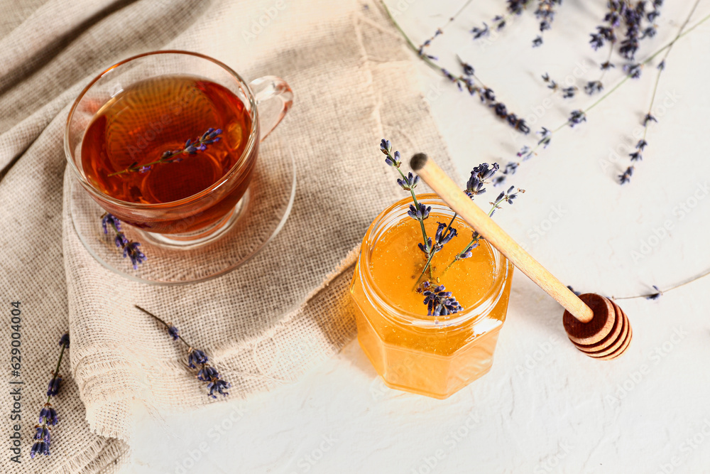 Jar with sweet lavender honey and cup of tea on white background