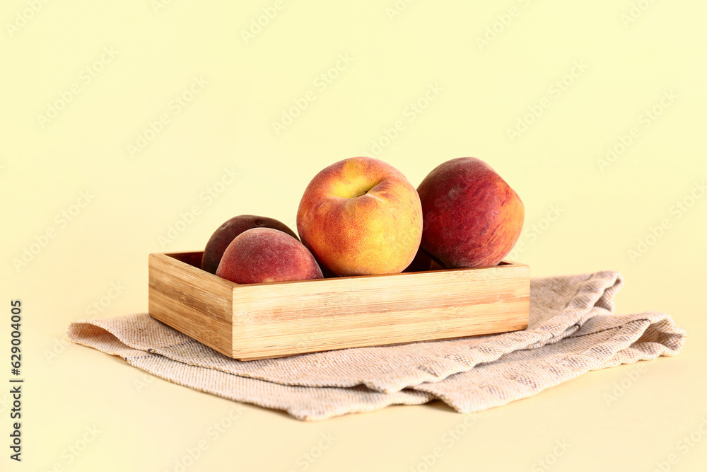 Wooden box with sweet peaches on yellow background