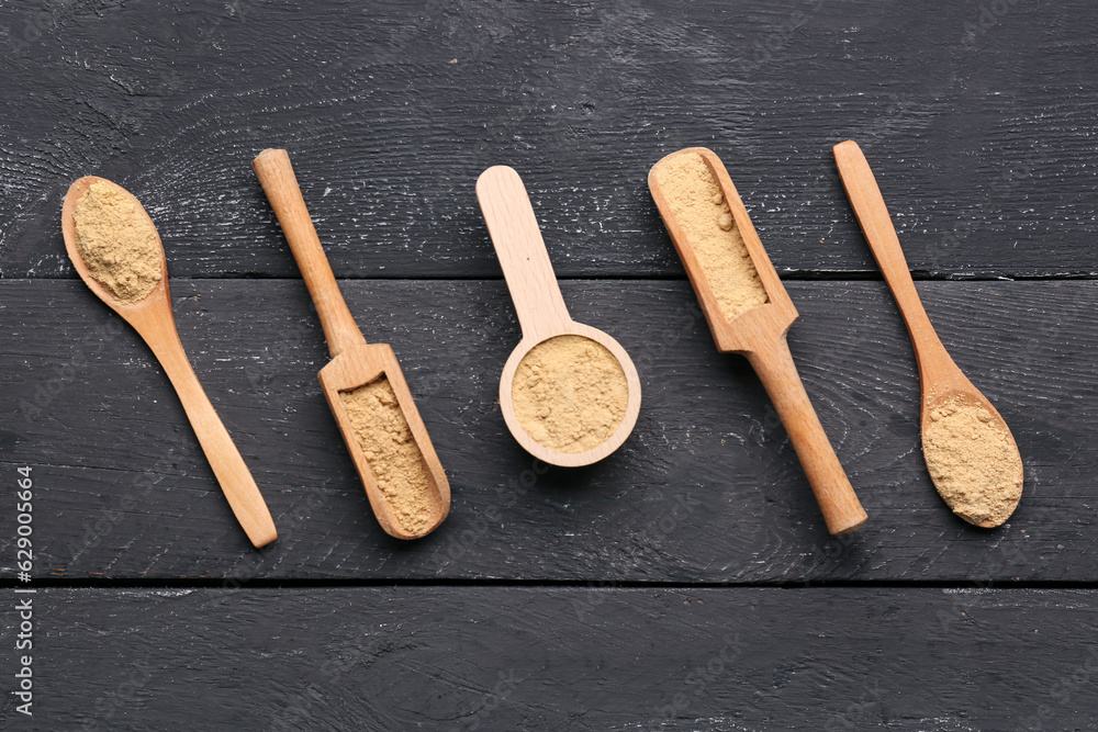 Spoons and scoops with ginger powder on black wooden background