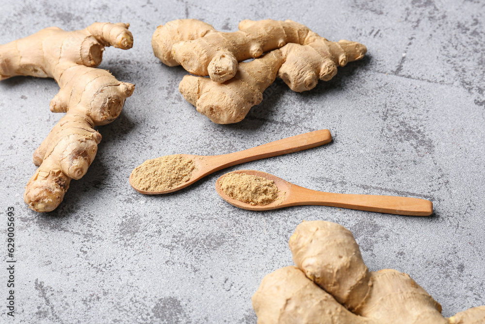 Fresh ginger roots and wooden spoons with dried powder on blue background