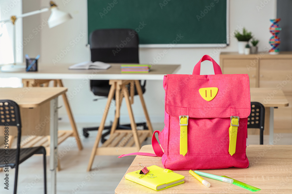 Pink school backpack with stationery on desk in classroom