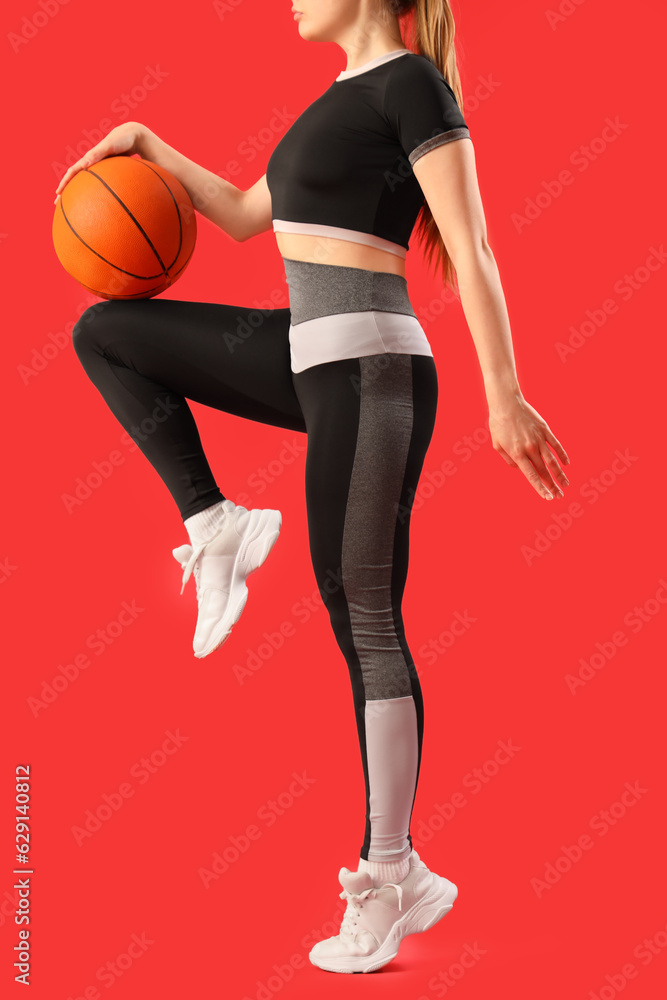 Young woman in sportswear and with ball on red background