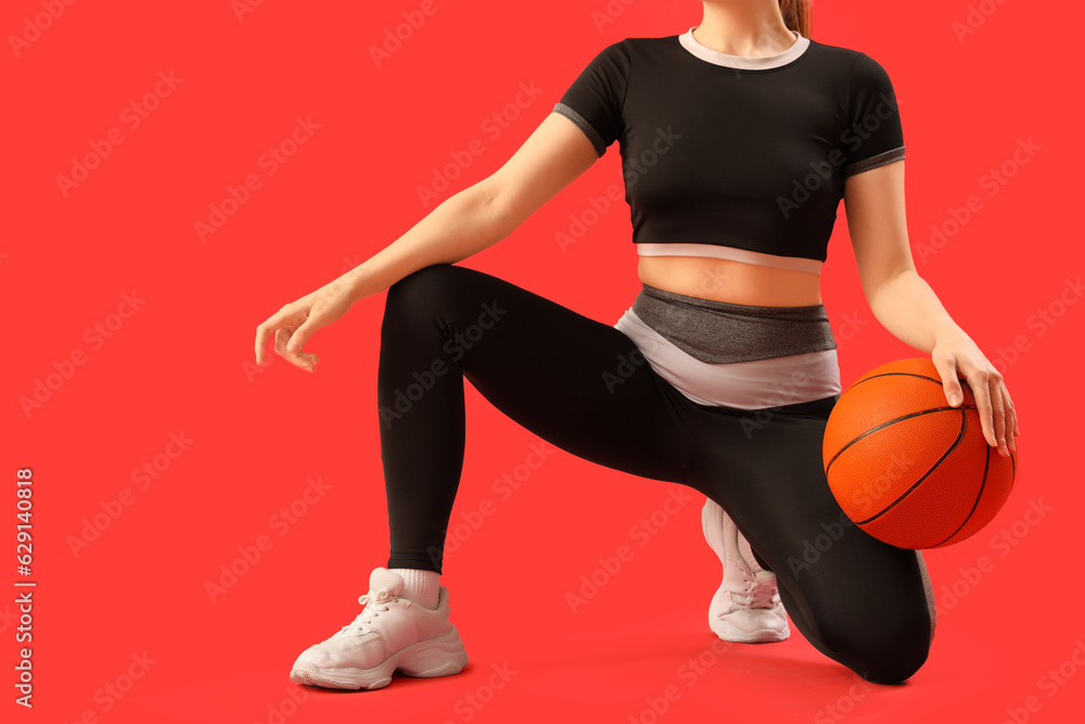 Young woman in sportswear and with ball on red background