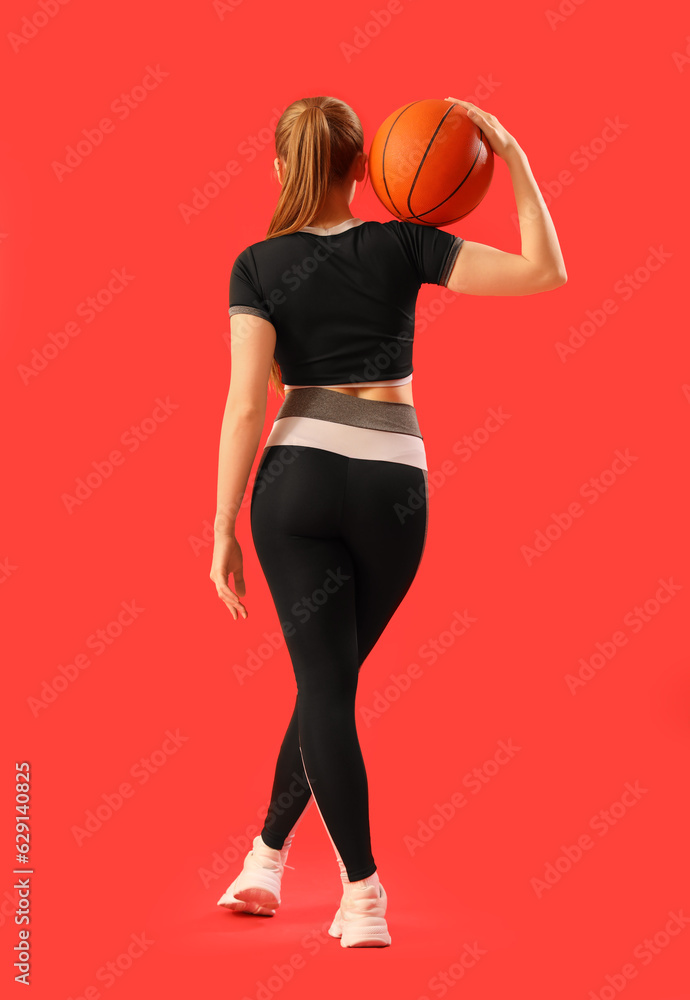 Young woman in sportswear and with ball on red background, back view