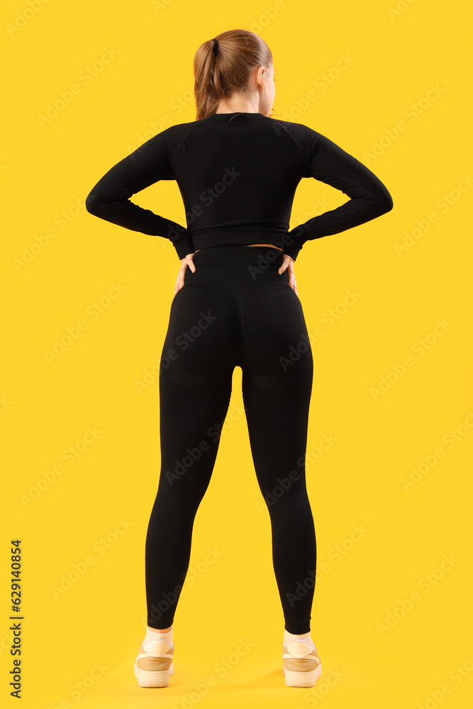 Young woman in sportswear on yellow background, back view