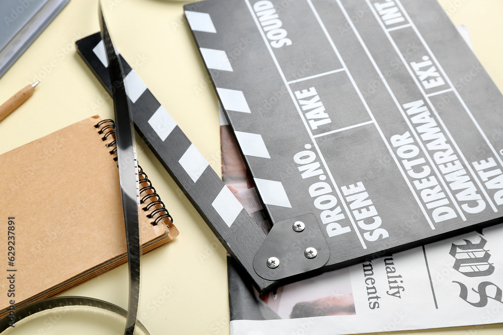 Movie clapper with newspaper, notebook and film on beige background, closeup