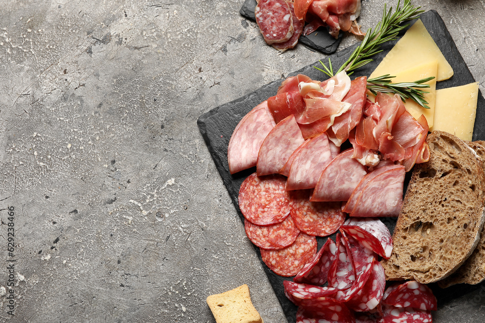 Slate plates with assortment of tasty deli meats, bread and cheese on grey background