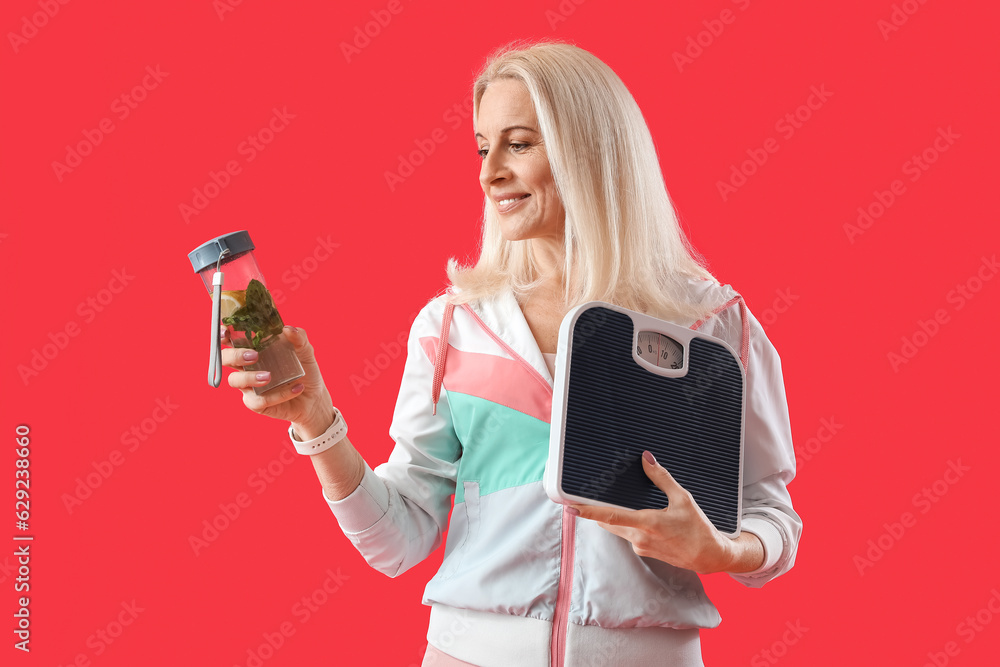 Sporty mature woman with scales and bottle of water on red background