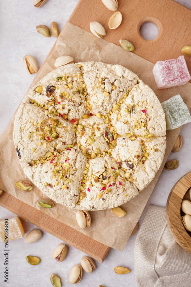 Wooden board of tasty Tahini halva with pistachios on light background