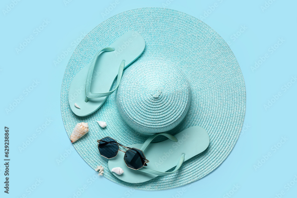 Flip-flops with sunglasses, seashells and hat on blue background