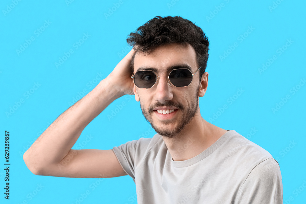 Young brunette man in sunglasses on blue background, closeup