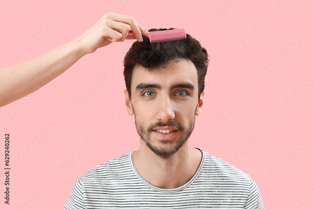 Female hairdresser combing hair of young man on pink background, closeup