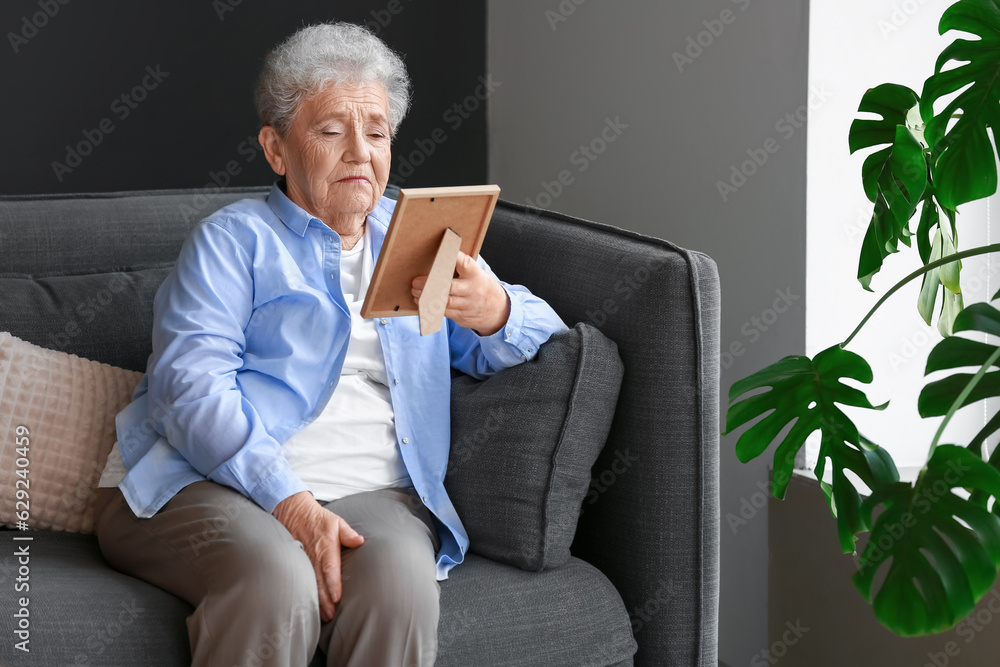 Senior woman with photo frame sitting on sofa at home