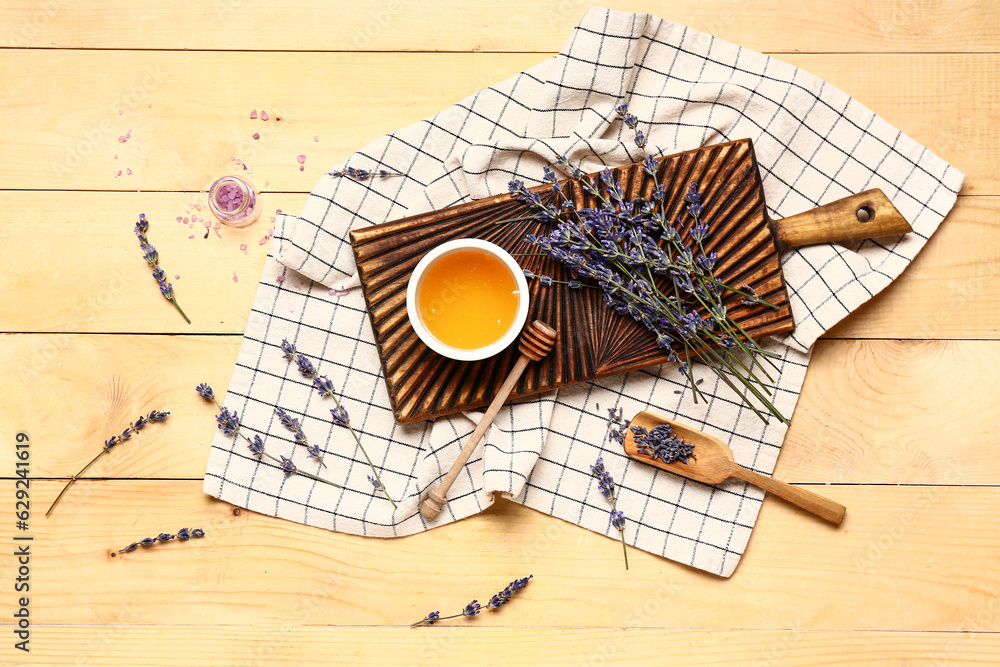 Board with bowl of sweet lavender honey, dipper and flowers on wooden background