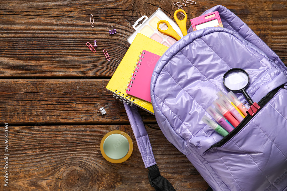 Lilac school backpack with bottle of juice and different stationery on wooden background