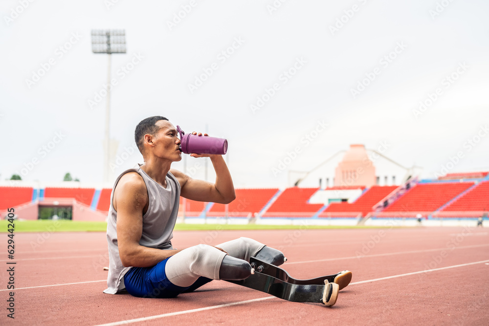 Asian para-athlete with prosthetic blades drinking water in stadium. 