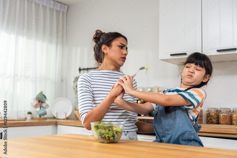 Caucasian mother teach and motivate young daughter eat green vegetable. 