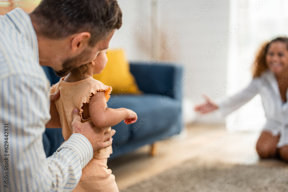 Caucasian baby girl child learn to walk with parents support in house. 