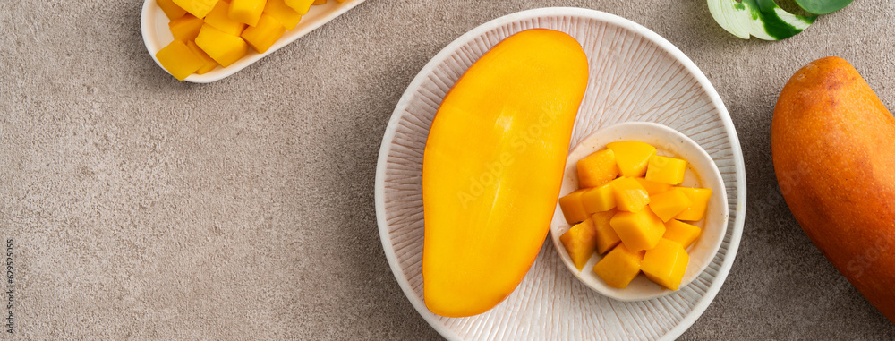 Fresh chopped, diced mango cubes on gray table background with tropical leaf.