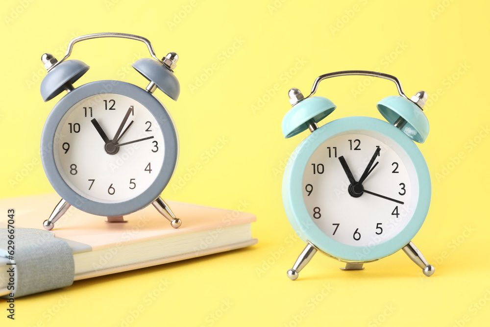 Alarm clocks and notebook on yellow background