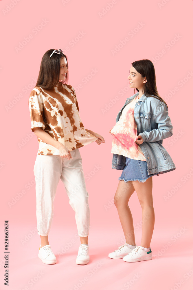 Stylish young women in tie-dye t-shirts on pink background