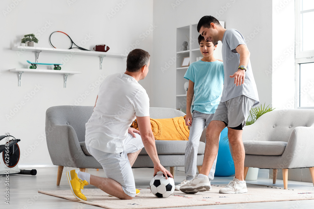 Happy young man with his little son and father playing football at home