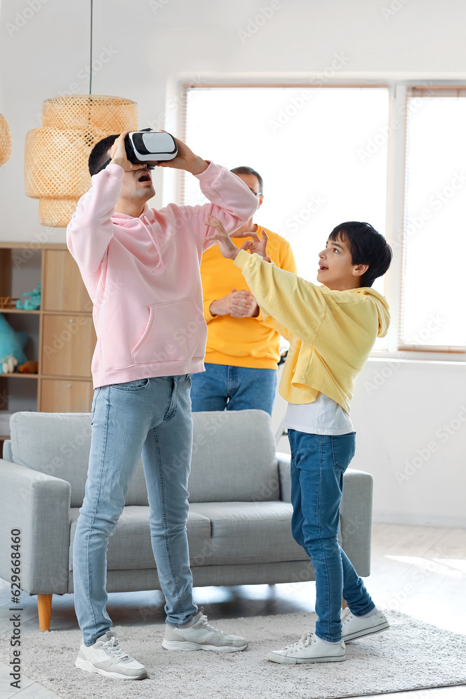 Young man with his little son and father using VR glasses at home