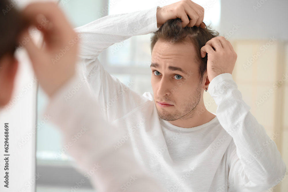 Young man with hair loss problem looking in mirror at home