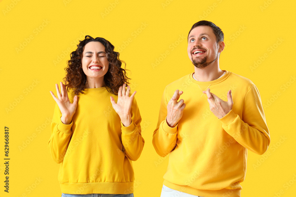 Happy young couple crossing fingers on yellow background