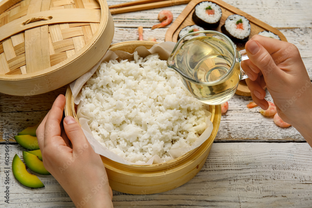 Woman adding vinegar into boiled rice on wooden table, closeup