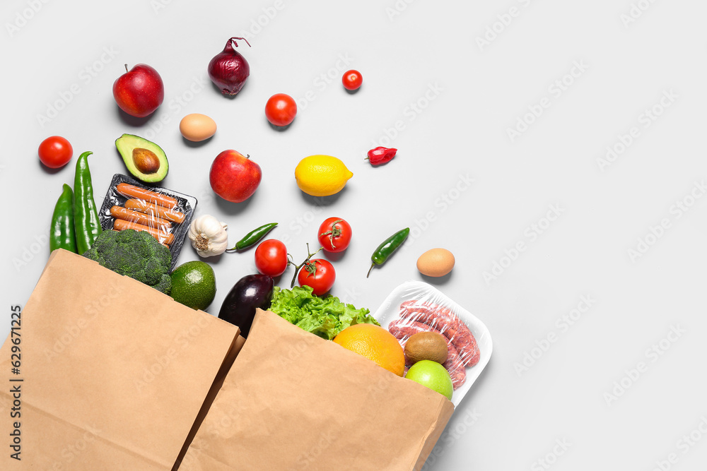 Paper bags with vegetables, fruits and sausages on grey background