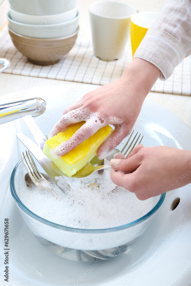 Woman washing spoon with sponge in sink, closeup