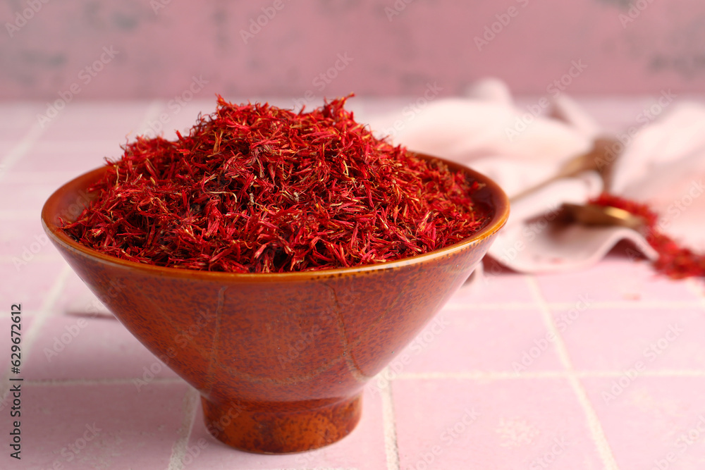 Bowl with pile of saffron on pink tile background