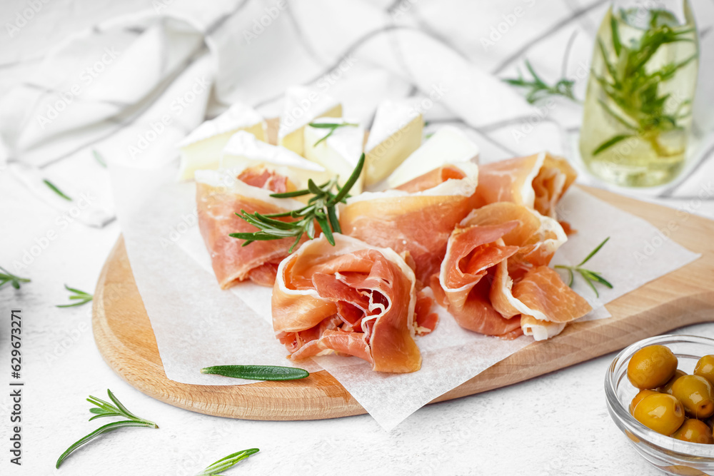 Wooden board with tasty jamon slices on light background