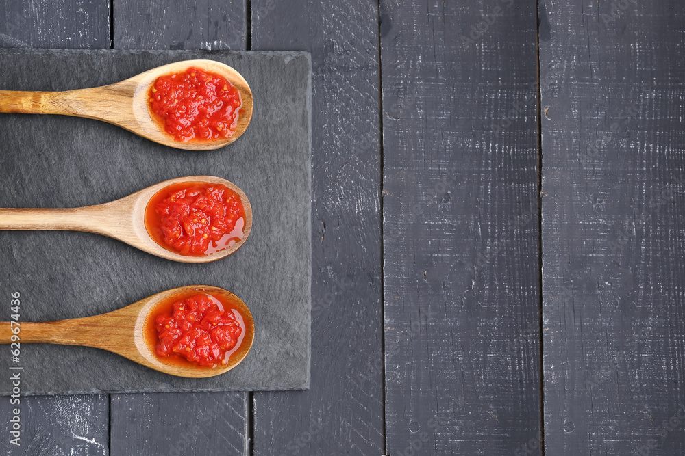 Spoons with tasty tomato sauce on black wooden background, closeup